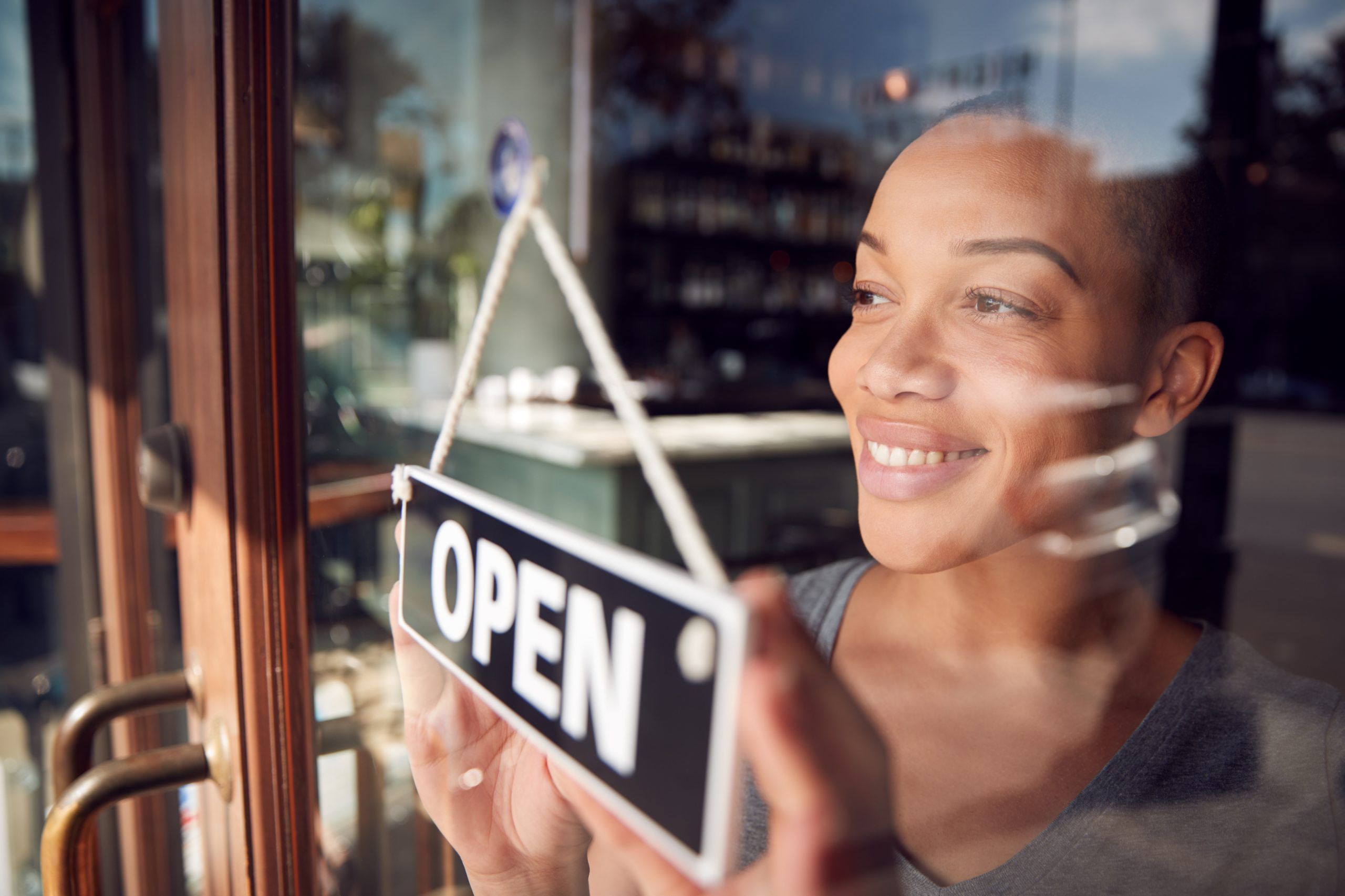 Smiling woman flipping open sign on door of business