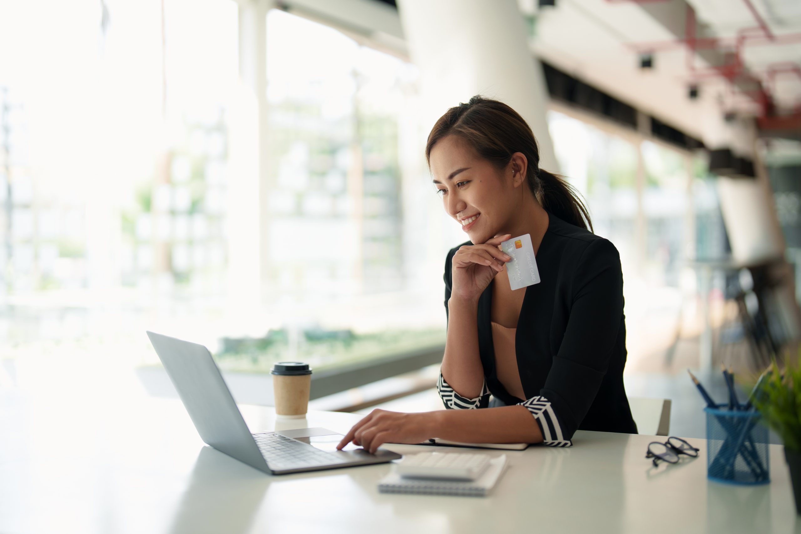 Woman smiling while holding bank credit card and using laptop